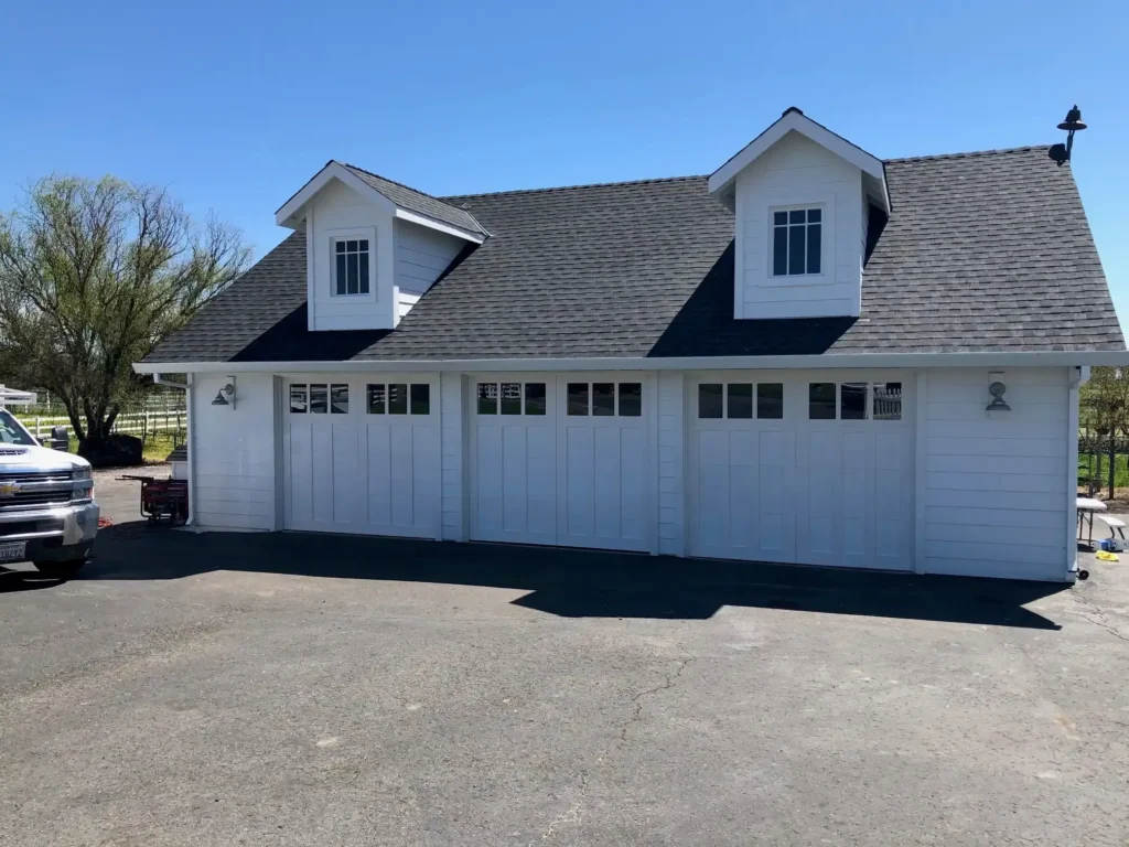 Three-car garage with white siding and dormer windows under a clear blue sky